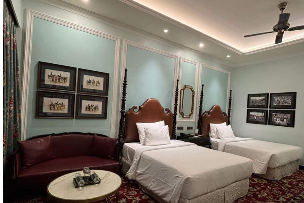 A hotel room with two beds, a red sofa, a round coffee table, and framed pictures on the walls.