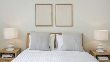 Una cama bien tendida con ropa blanca, flanqueada por dos mesitas de noche con lámparas y libros.