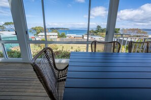 Una terraza de madera con sillas de mimbre y una mesa, con vistas a la costa, casas y al mar.
