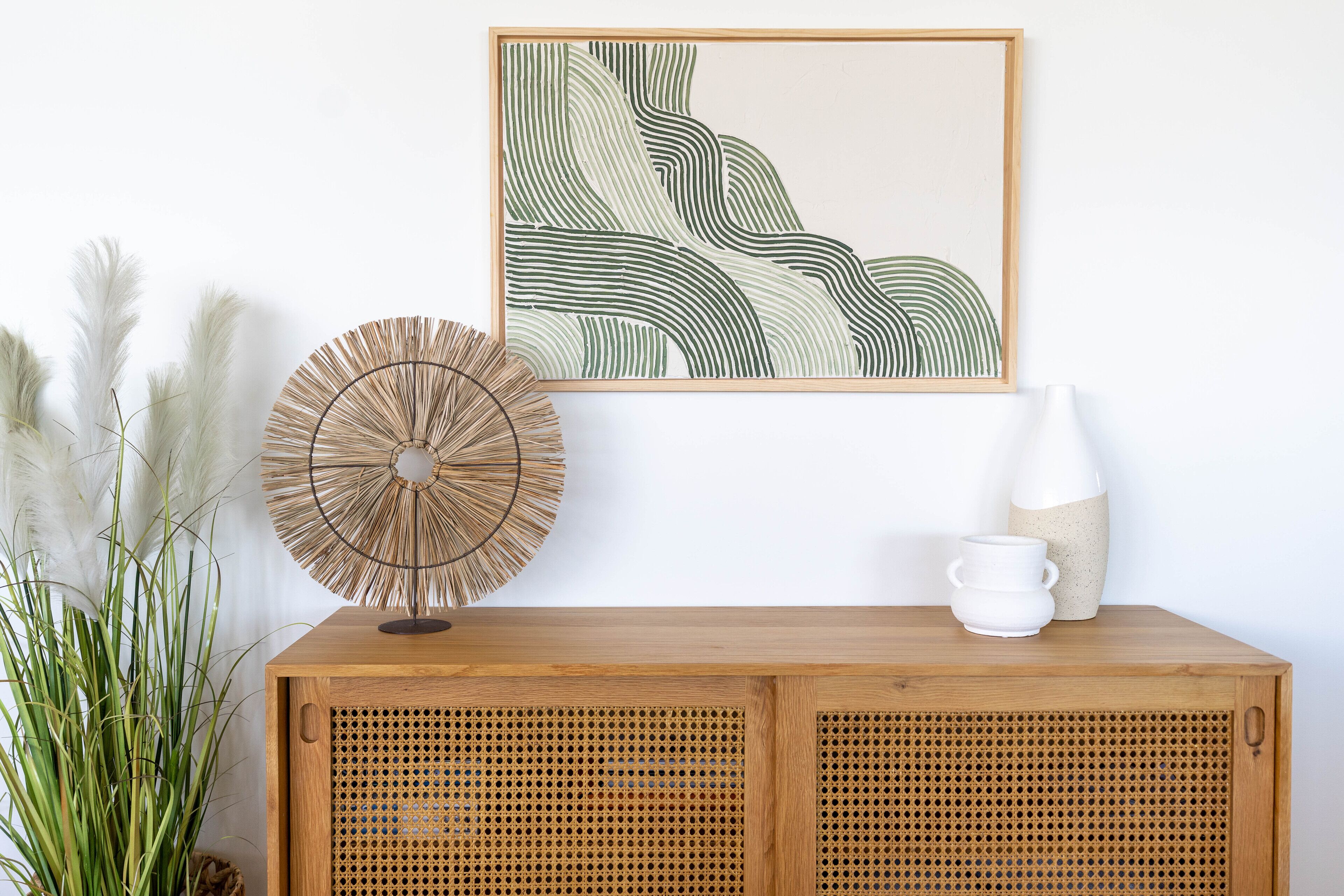 A wooden cabinet with a woven basket and a framed abstract painting.
