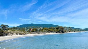 A beach with clear blue water, sandy shore, and a forested hill in the background. - Blue Cottage Bruny Island (Alonnah)