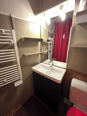 A bathroom with a white sink, a mirror, a towel rack, and a red shower curtain.