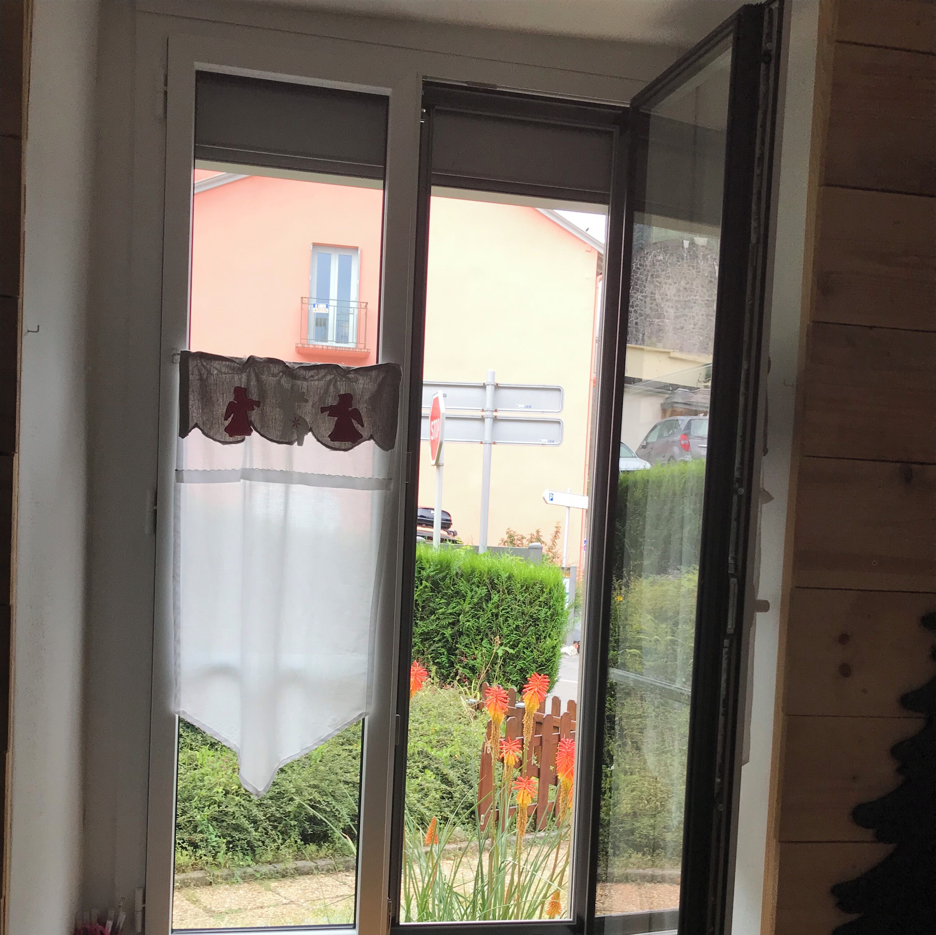 Une porte avec un rideau blanc et une petite fenêtre donnant sur un jardin et un bâtiment.