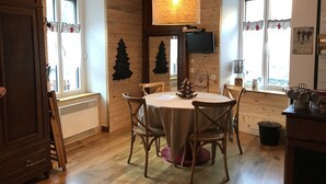 A dining area with a round table, wooden chairs, a hanging light fixture, and a wooden wall with decorations.
