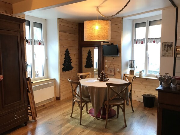 A dining area with a round table, wooden chairs, a hanging light fixture, and a wooden wall with decorations.