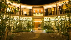 Un hotel de varios niveles con un patio central, rodeado de plantas de bambú e iluminado con luz cálida.