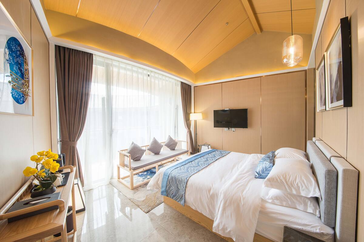 Una habitación de hotel moderna con una cama grande, un televisor montado en la pared y una zona de estar con vistas a la ciudad.