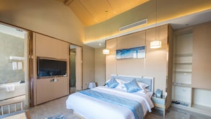 Una habitación de hotel moderna con una cama grande, televisión y un baño visible a través de una puerta abierta.