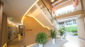 Un moderno vestíbulo de hotel con una escalera de madera, plantas en macetas y vistas al jardín exterior.