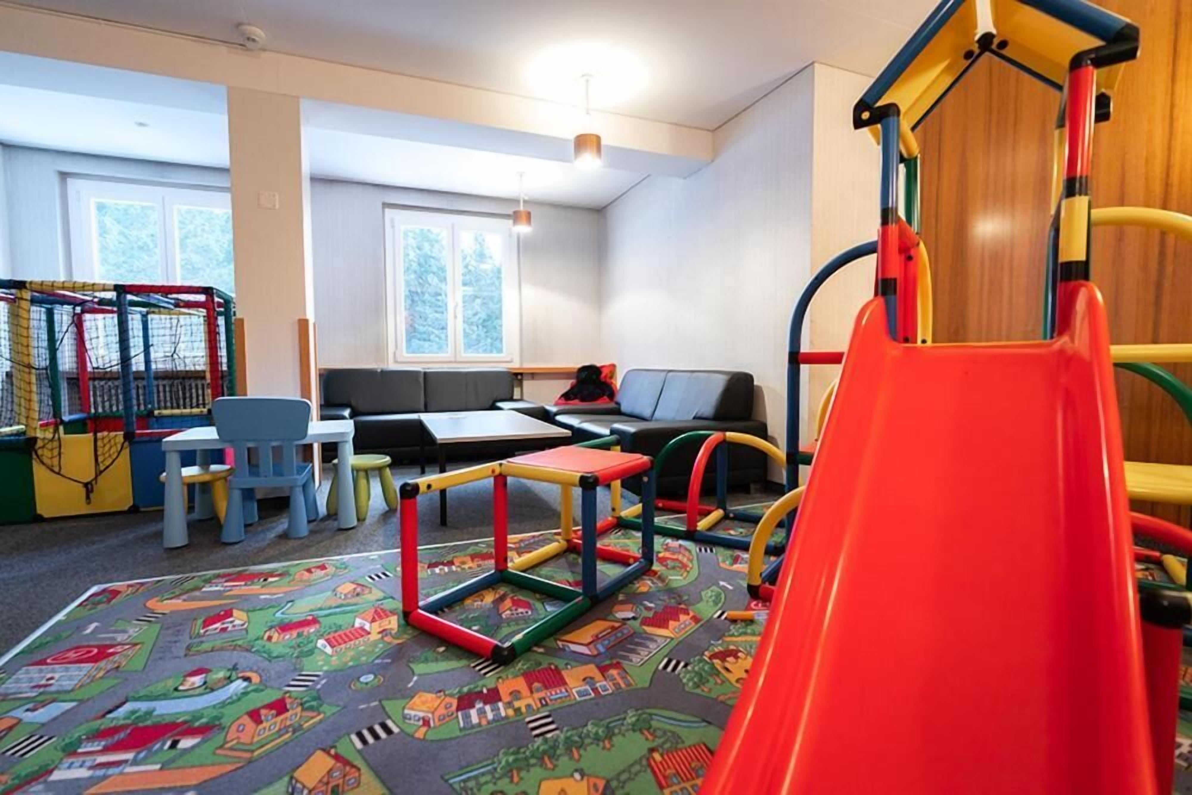 Une salle de jeux avec une structure colorée, un toboggan et un espace détente comprenant un canapé et des tables.