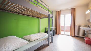 Ein Mehrbettzimmer mit einem grünen Wand, einem Fenster mit Vorhängen, einem Heizkörper und einem Waschbecken.