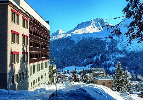 A modern building with multiple windows and balconies, surrounded by snow-covered mountains and trees. - Arosa Mountain Lodge (Arosa)