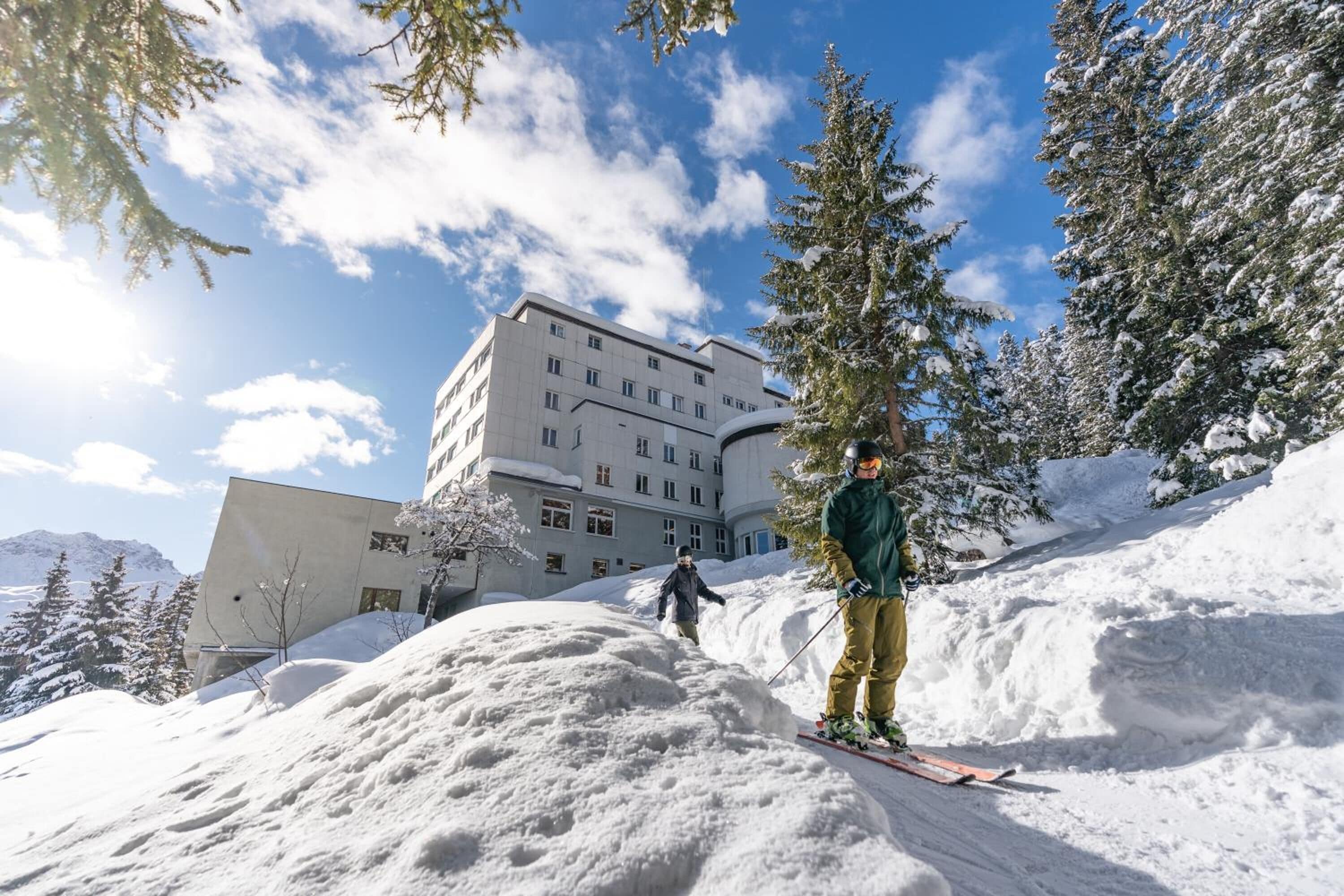 A ski resort with a large building in the background, snow-covered trees, and a clear sky.