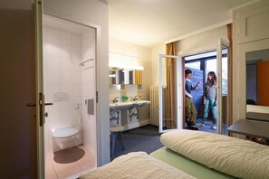 A hotel room with a bathroom, a double bed, a bedside table, and a window with curtains. - Arosa Mountain Lodge (Arosa)
