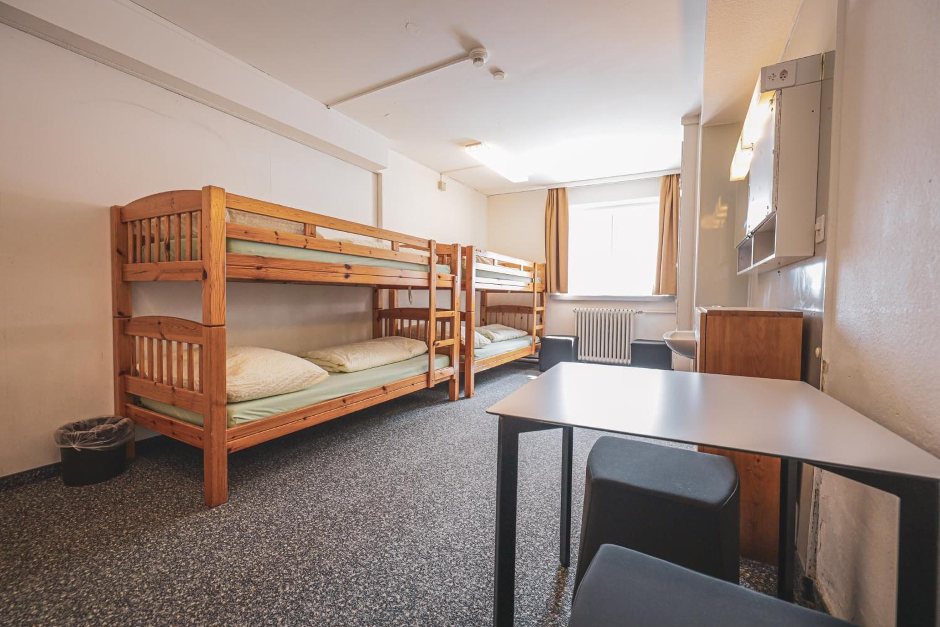 A dormitory room with bunk beds, a table, and chairs.