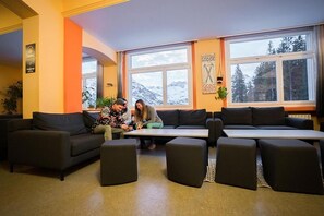 A modern interior with a sofa set, a coffee table, and a large window with a mountain view. - Arosa Mountain Lodge (Arosa)