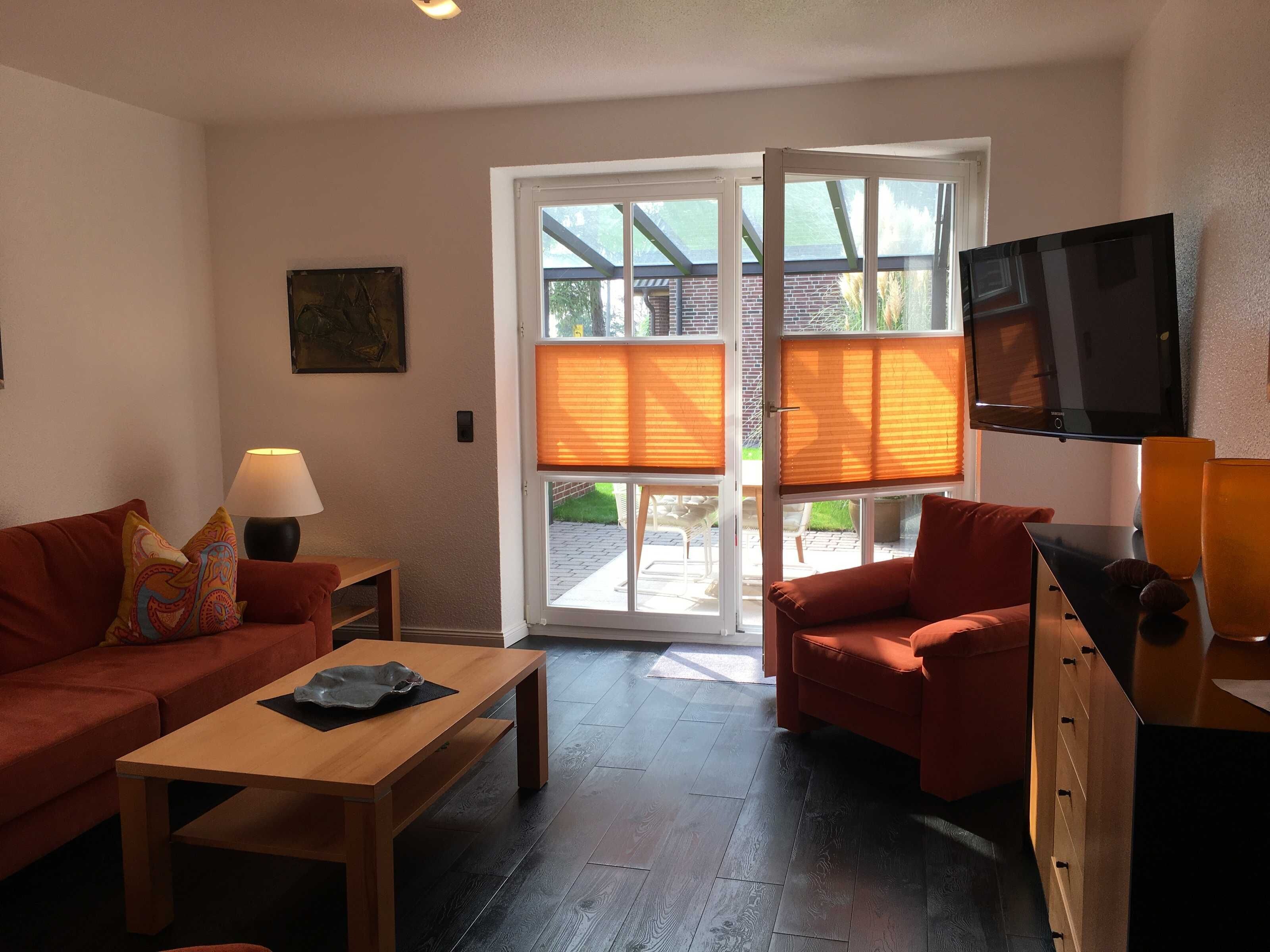 Een woonkamer met een bank, een salontafel, een televisie en een schuifpui die leidt naar een buitenruimte.