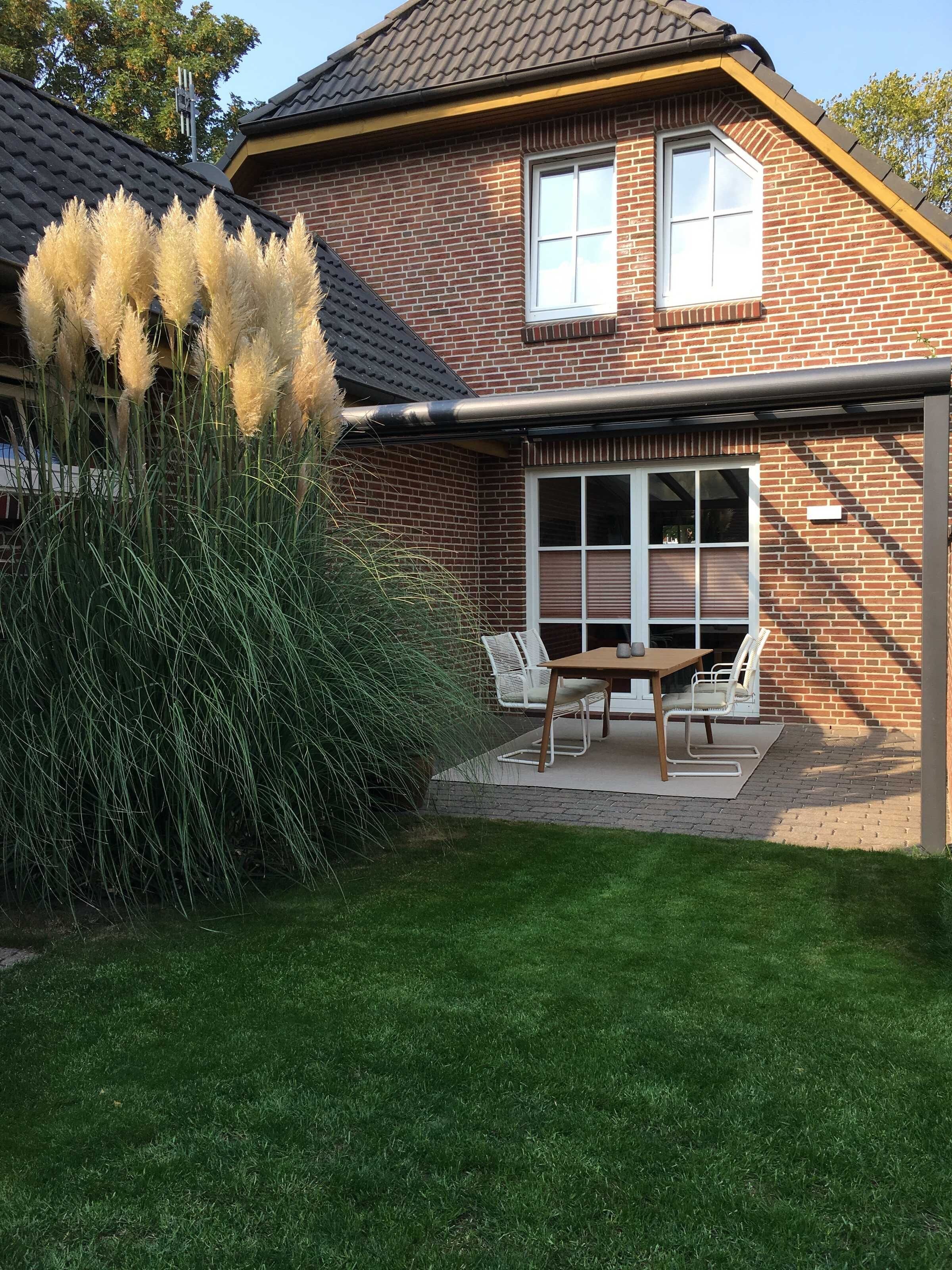 A two-story house with a brick exterior, a covered patio with outdoor furniture, and a well-maintained lawn.