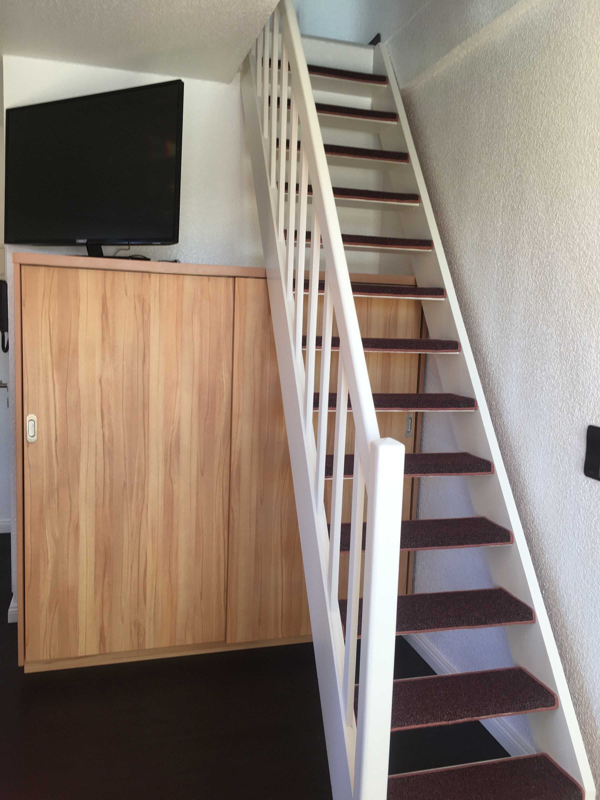 Un escalier avec des rampes blanches et une armoire en bois sur laquelle est posée une télévision.