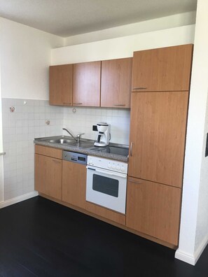 A kitchen with wooden cabinets, a built-in oven, a coffee maker, and a dishwasher. - Boje - Villa an der Au (Fehmarn)