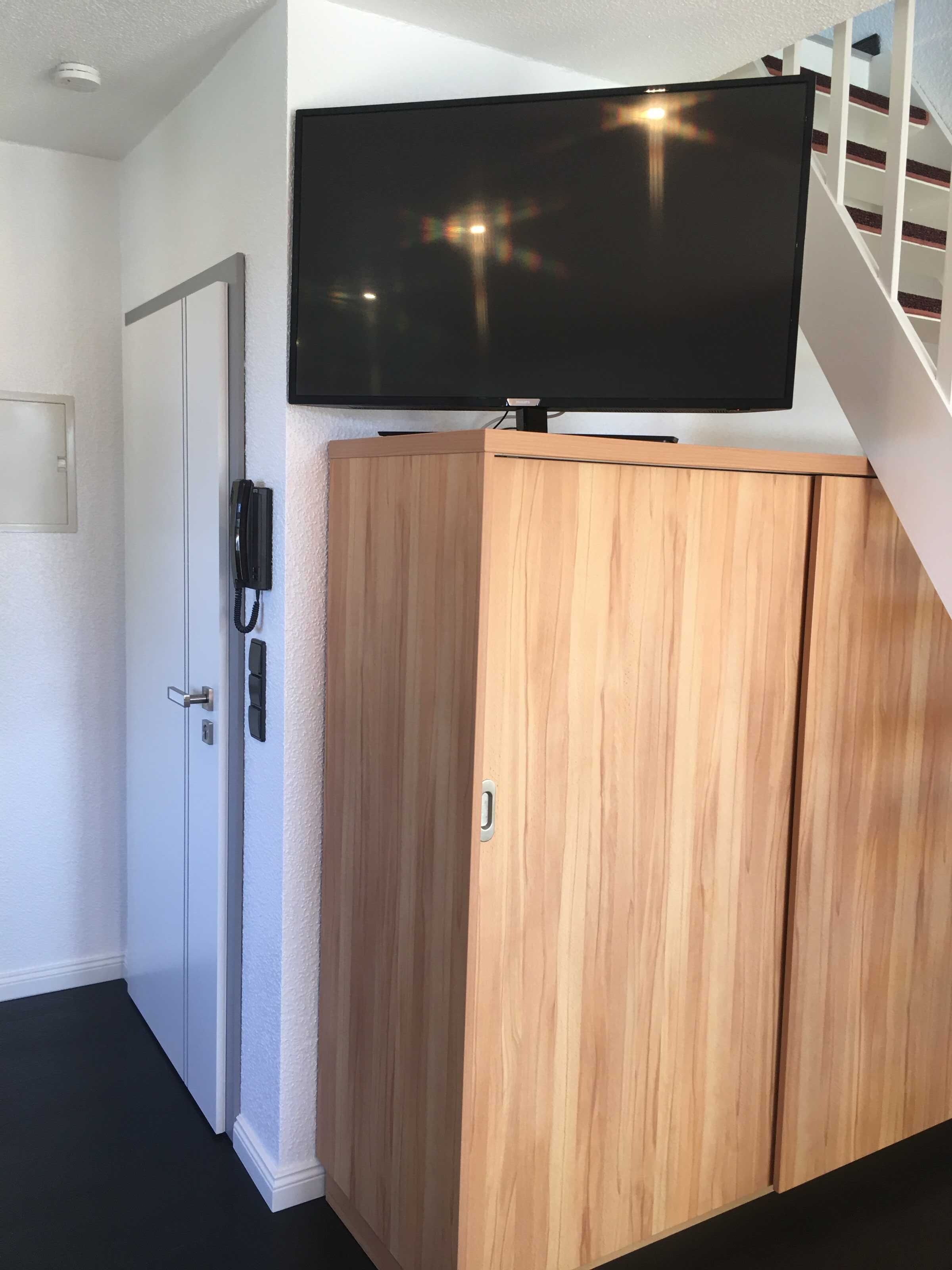 Ein Zimmer mit einem Holzschrank, einer weißen Tür, einem fest installierten Telefon und einem Fernseher auf einem Schrank.