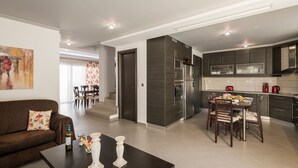 Eine moderne Küche mit dunklen Schränken, ein Essbereich mit Tisch und Stühlen sowie ein Wohnzimmer mit Sofa und Couchtisch.