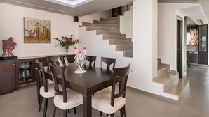 Ein moderner Essbereich mit einem dunklen Holztisch und -stühlen, einer Glaskabine mit Regalen sowie einer minimalistisch gestalteten Treppe.