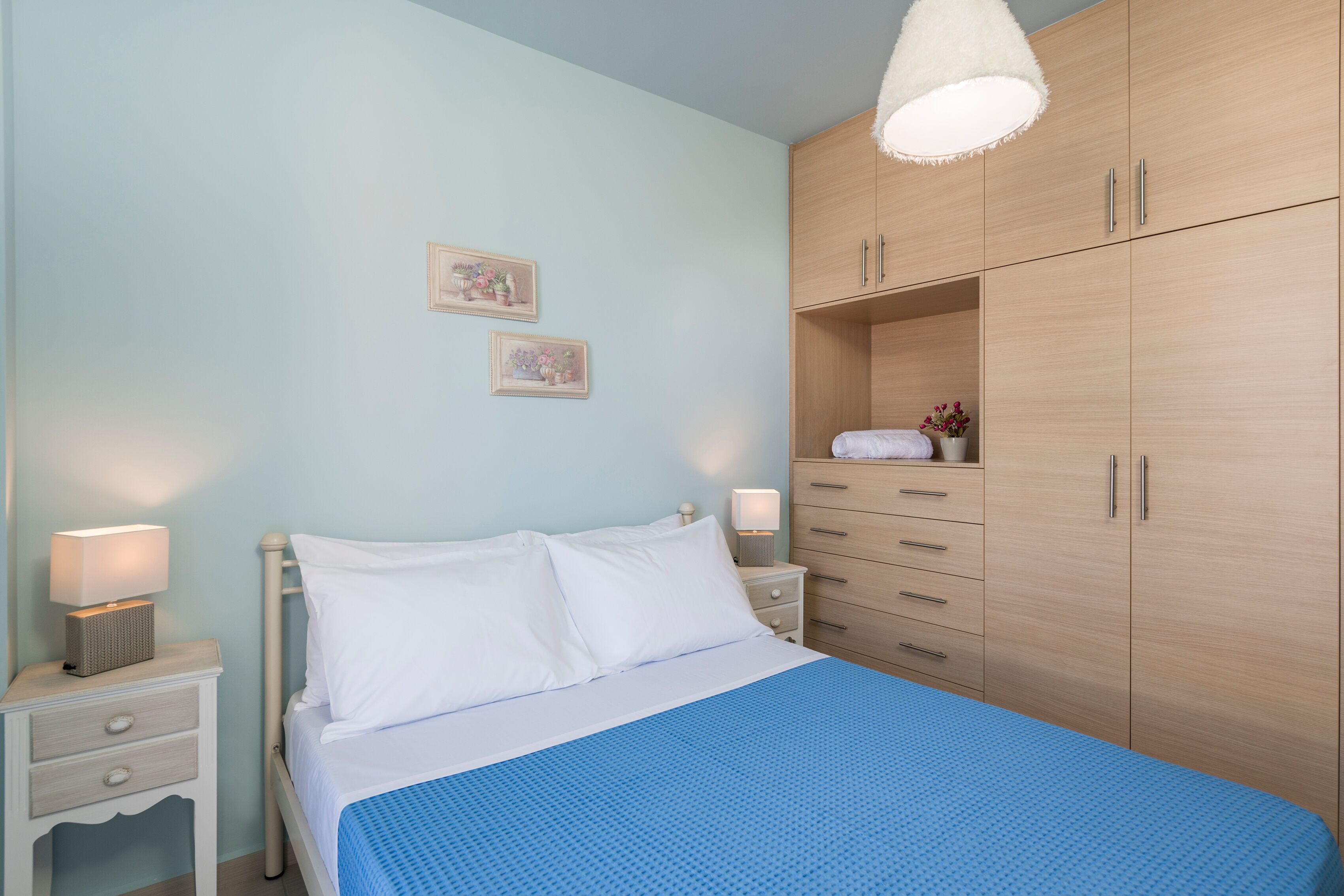 A bedroom with a bed, a nightstand, a dresser, and a hanging light fixture.