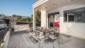 Eine überdachte Terrasse mit Tisch, Stühlen und einer Bank, mit Blick auf die Straße.