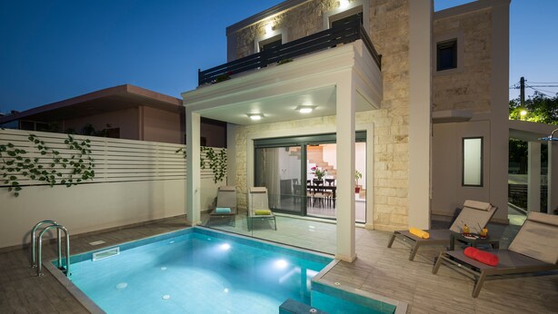 Ein moderner Außenpool mit Glasveranda, angrenzende Liegestühle und ein Steinhaus mit Balkon.