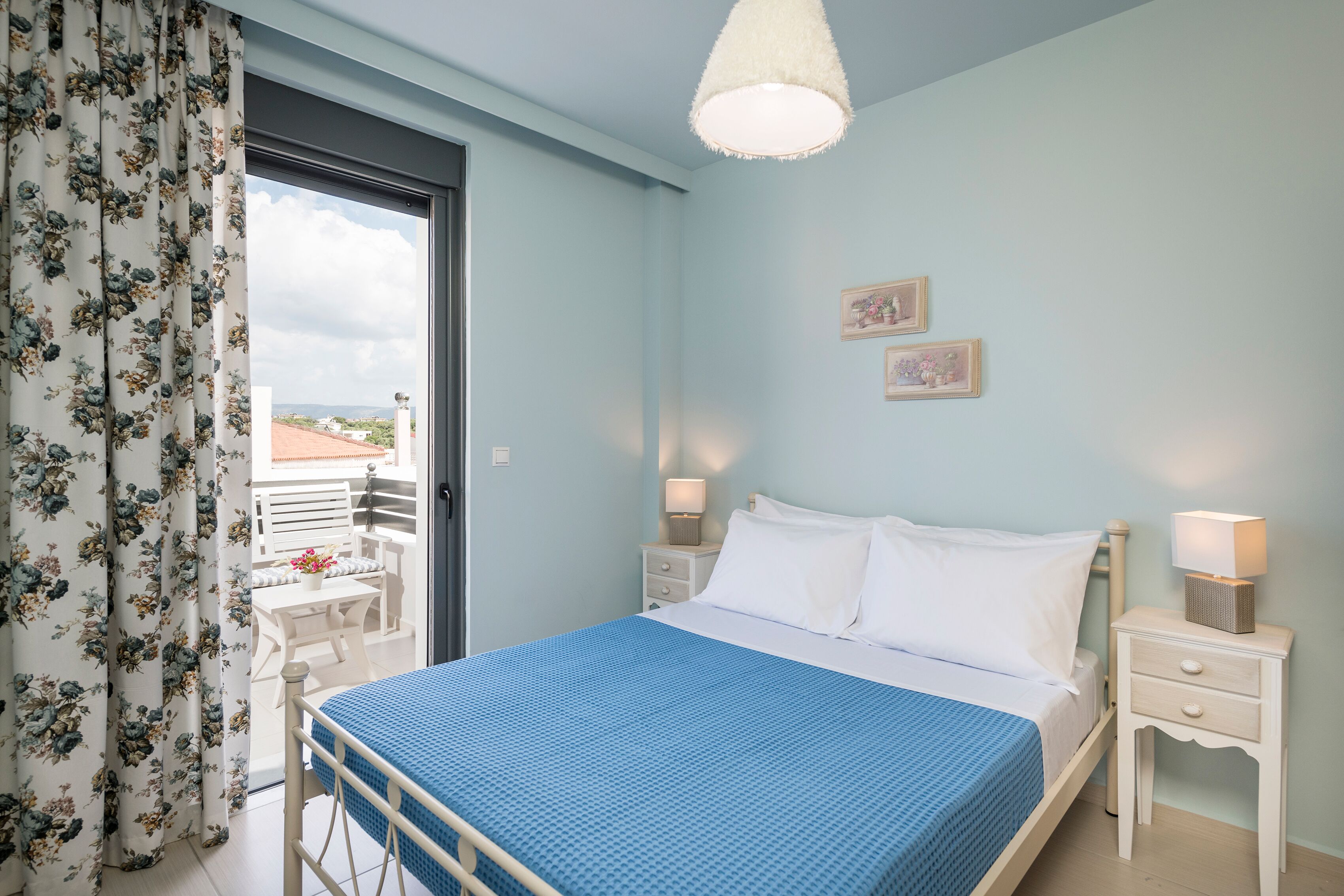 Un dormitorio con cama, dos mesitas de noche, una ventana con cortinas y un balcón.