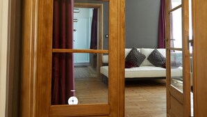 Un chambranle en bois encadre une porte qui donne sur une pièce où se trouve un canapé blanc et des coussins à motifs.