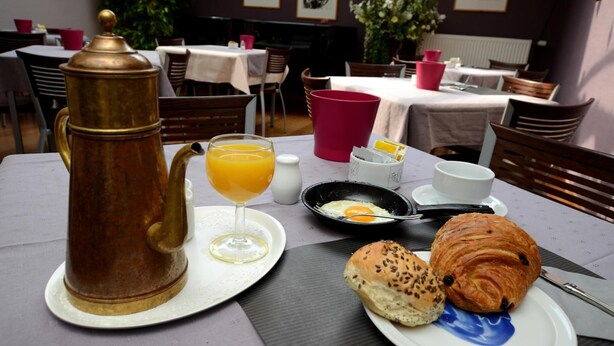 Une table dressée pour le petit-déjeuner, avec une cafetière, du jus d’orange, des œufs, des croissants et un muffin.