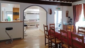 Un coin repas avec des chaises en bois et une nappe rouge, une cuisine avec des meubles blancs et un plafond en bois.