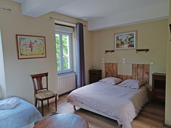 Ein Schlafzimmer mit einem großen Bett, einem Sessel, einem Fenster mit Vorhängen und zwei an der Wand befestigten Bildern.