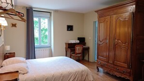 Une chambre à coucher comprenant un lit, une armoire en bois, un bureau avec une chaise, un radiateur et une fenêtre avec des rideaux.