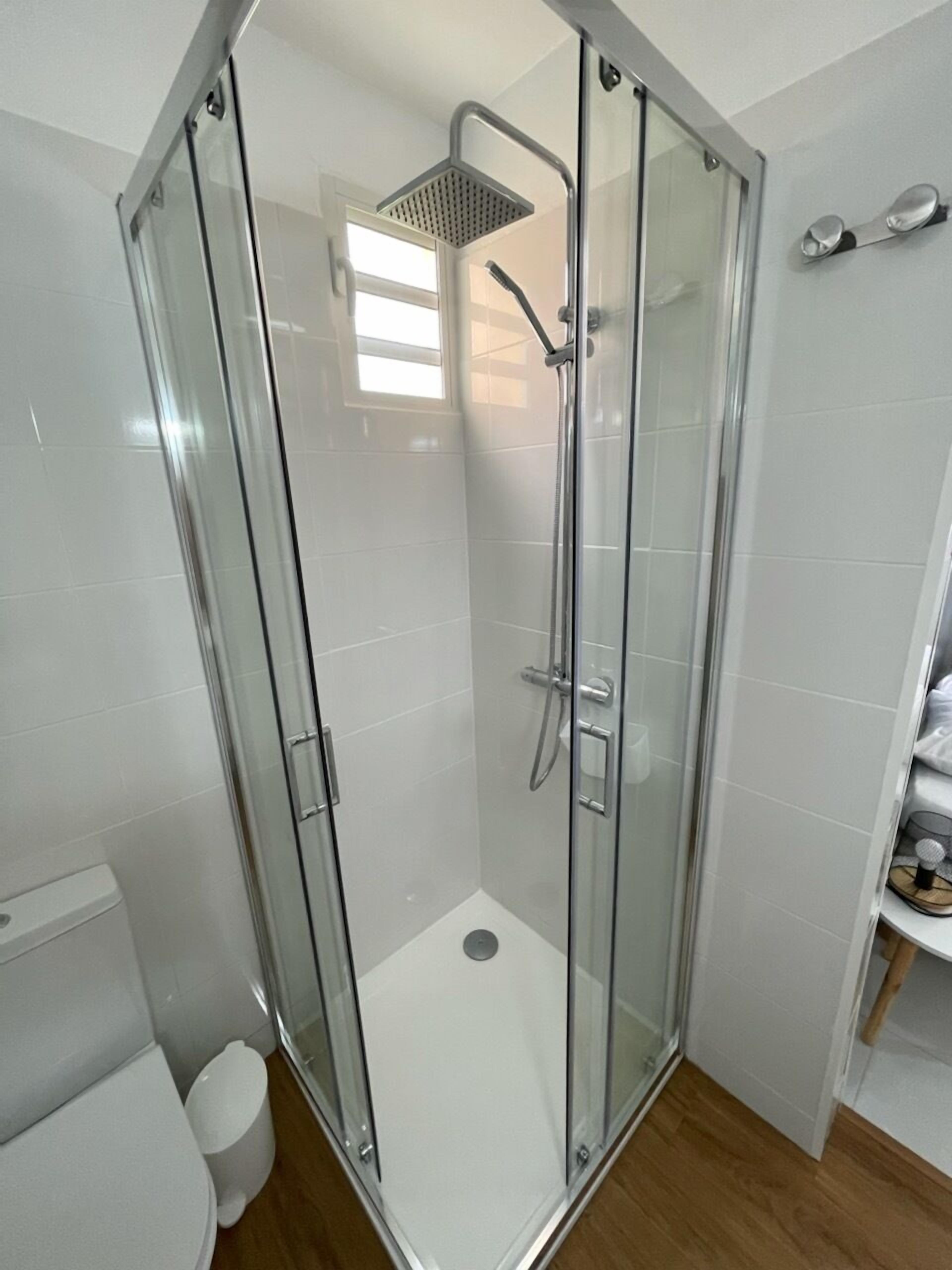 Ein modernes Badezimmer mit einer Duschkabine aus Glas, weißen Fliesen und Holzboden.