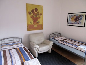 Une chambre avec deux lits simples, une chaise et deux tableaux accrochés aux murs.