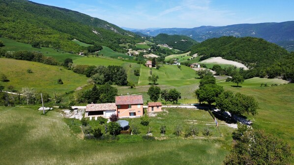 A rural landscape with rolling hills, a farmhouse, and scattered trees.