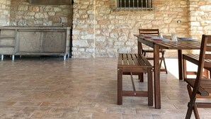 Una cocina rústica con paredes de piedra y vigas de madera, un comedor con mesa y sillas, y una lámpara colgante.