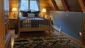 Un dormitorio acogedor en el ático, con techo de madera, una cama con cabecera, una ventana con cortinas y una alfombra estampada.