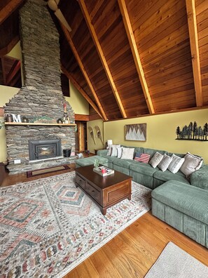 Una sala de estar acogedora con chimenea de piedra, vigas de madera, un sofá verde y un tapete estampado.