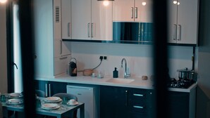 A compact kitchen with white cabinets, a sink, and a stove. There is a dining table with plates and glasses. - Aden Life (Ankara)