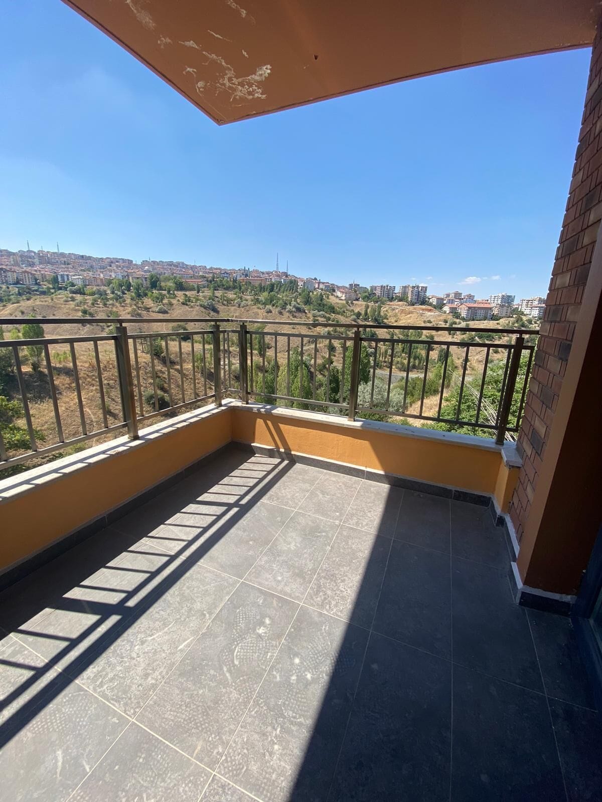 Uma varanda com vista para a cidade, com piso de azulejos e corrimão de metal.
