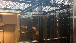 An elevator interior with a patterned ceiling and reflective glass walls. - Aden Life (Ankara)