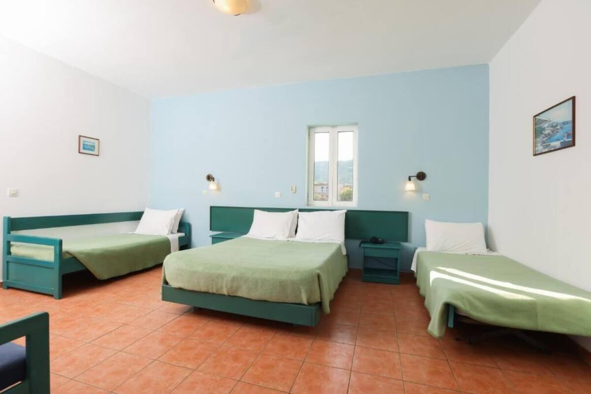 A room with three single beds, a window, and two wall-mounted lamps.