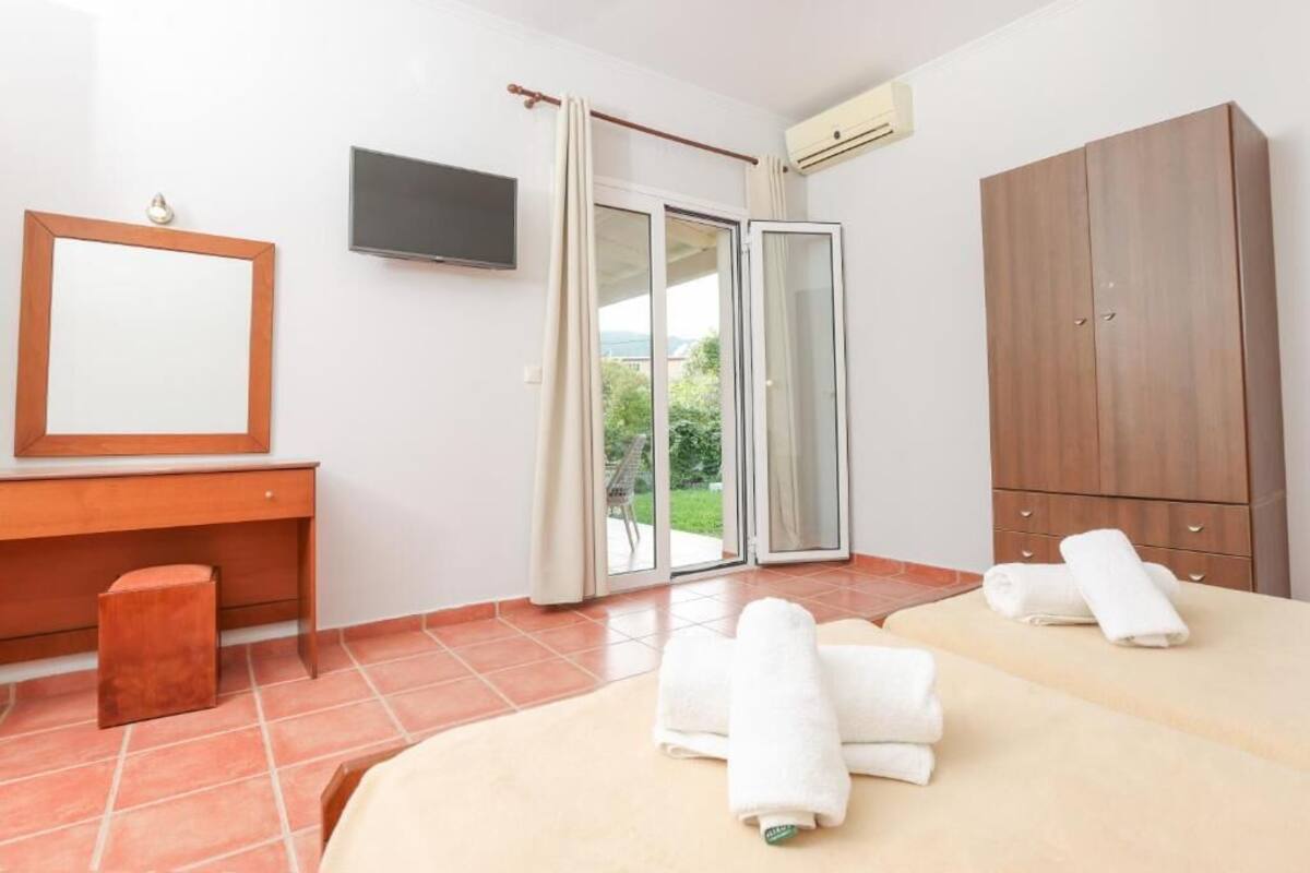 A bedroom with a bed, a desk, a wardrobe, a TV, and a sliding glass door leading to a balcony.