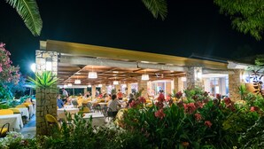 Un espacio de comedor al aire libre con pilares de piedra, sillas amarillas y mesas bajo techo.
