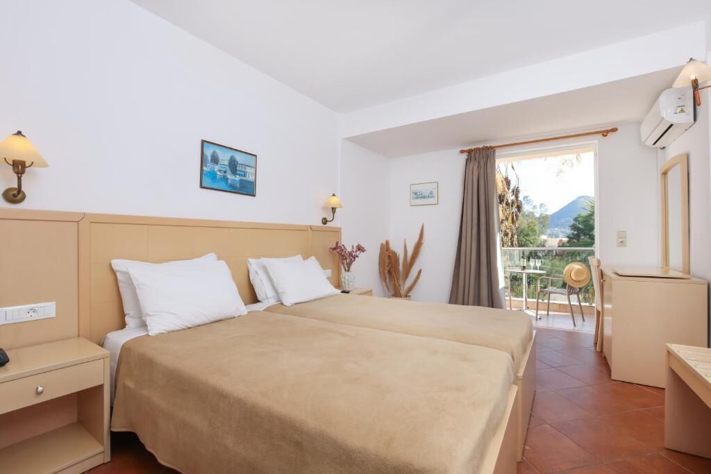 Ein Hotelzimmer mit zwei Betten, einem Balkon mit Aussicht und einem Schreibtisch mit Stuhl.