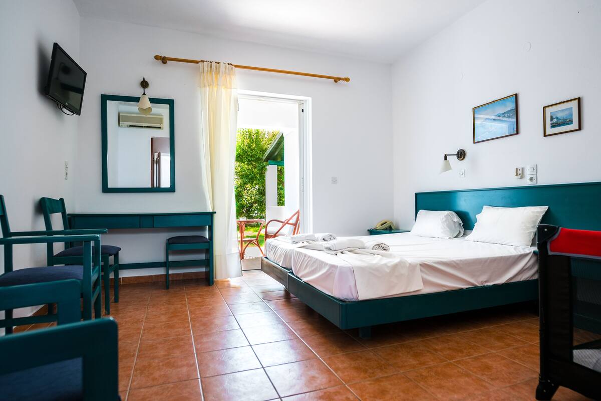 A bedroom with a bed, desk, chairs, and a TV.